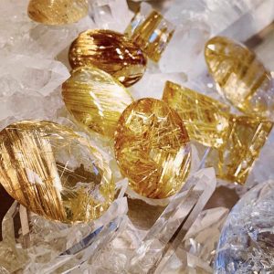 Ảnh cận cảnh các viên đá Vòng Thạch Anh Tóc Vàng SOLUNA (Rutilated Quartz) cao cấp. Viên đá có tinh thể trong suốt và các sợi Rutile vàng kim dày đặc, làm nổi bật chất lượng SOLUNA để chiêu tài lộc và năng lượng thịnh vượng.